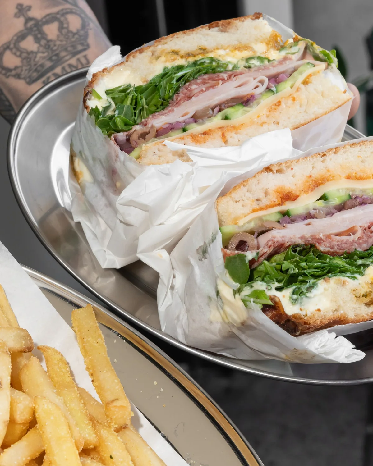 Two focaccias cut open in deli paper on a steel tray, with fries beside them